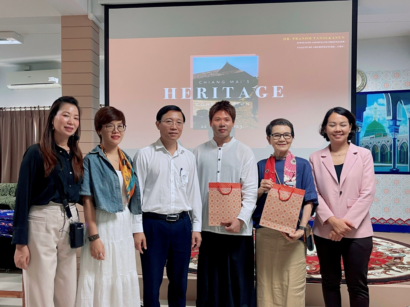 A group of people standing in front of a projector screen Description automatically generated