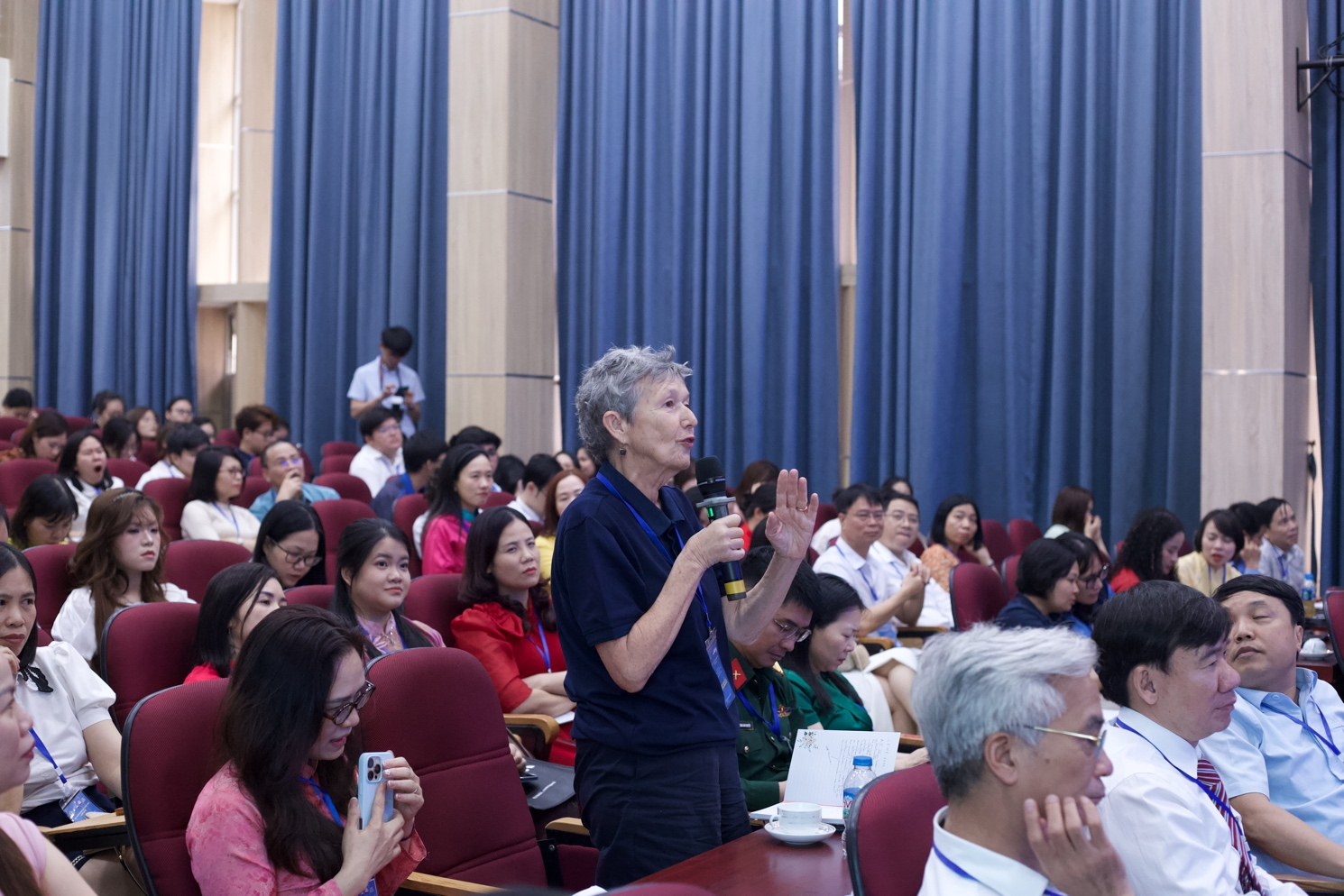 A person speaking to a group of people in a lecture hall Description automatically generated