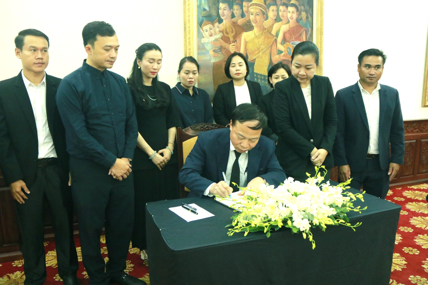 A group of people standing around a person signing a document Description automatically generated