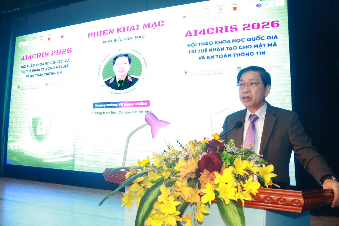 A person standing at a podium with a large screen Description automatically generated